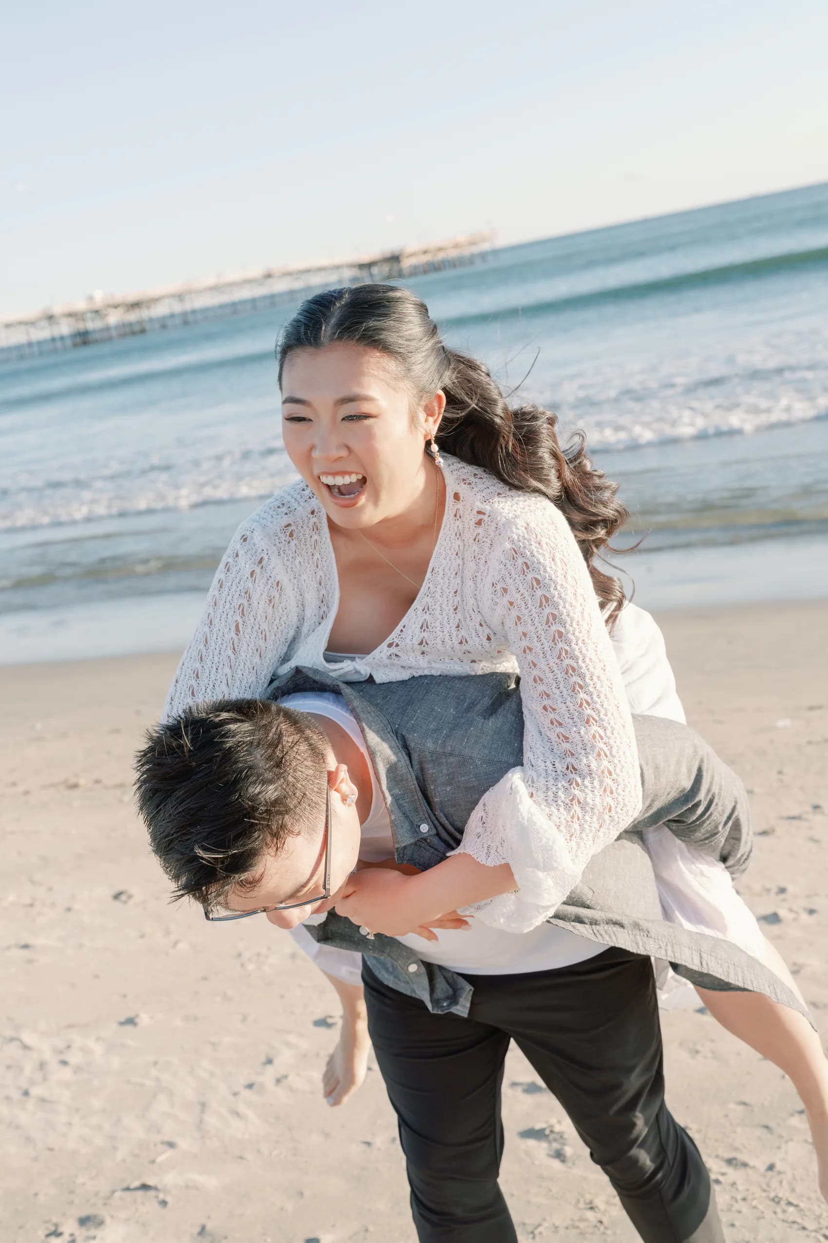 Christine laughing while riding on Thomas's back at the beach