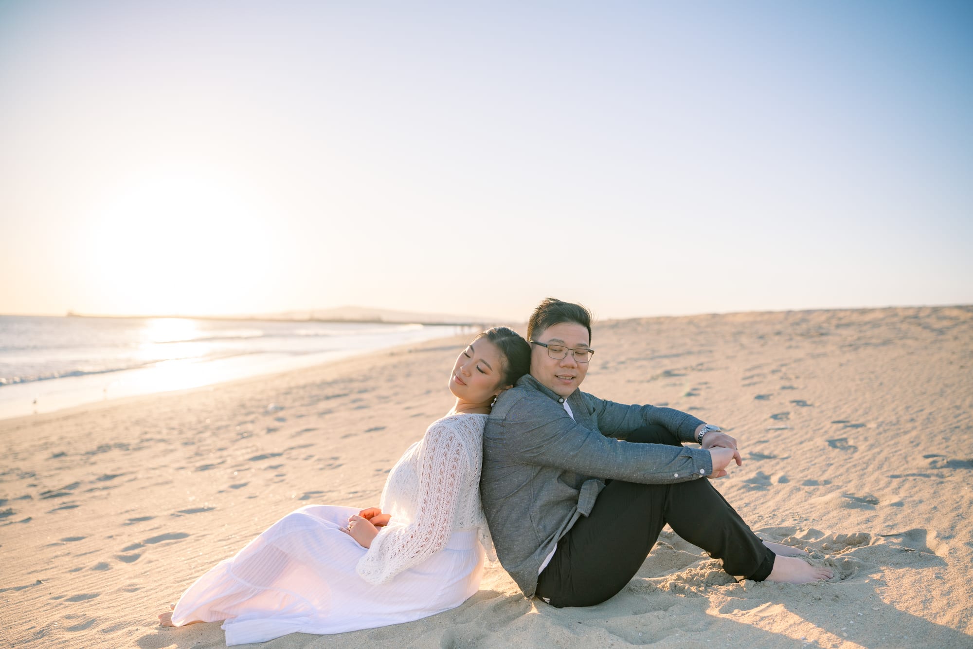 Christine and Thomas sitting on the sand at sunset.