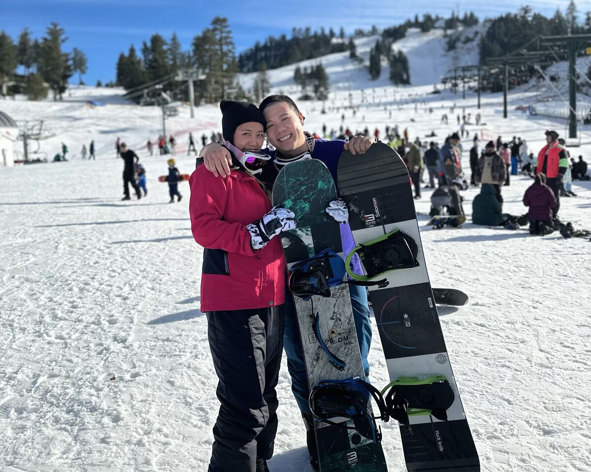 Christine and Thomas on a snowy slope, holding a snowboard.